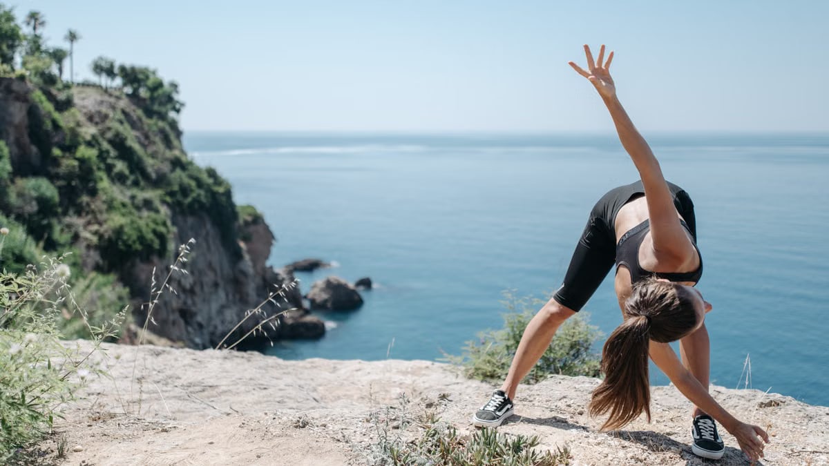 A woman in activewear stretching on a cliff with a stunning ocean view, embracing a fitness lifestyle.